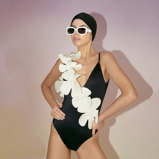 Light pink one-piece bikini with large cream floral appliques on the left shoulder and torso, worn by a woman.