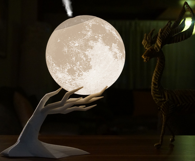 Moon-shaped humidifier and night light with a white deer stand, emitting mist, on a wooden table with books. - Image 11