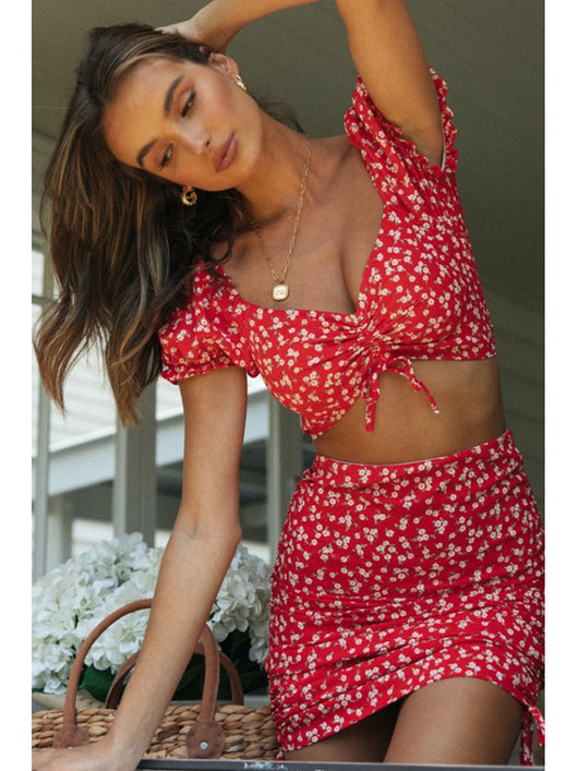 Smiling woman in a red floral print crop top and matching ruched mini skirt with side ties. - Image 12