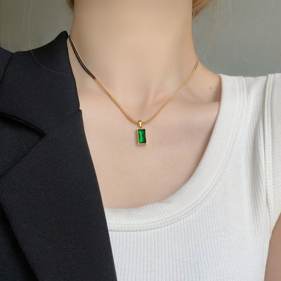 Gold hoop earrings with rectangular emerald green zircon pendants, displayed on a light beige fabric. - Image 10