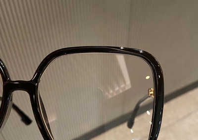 Black oversized square anti-blue light glasses with clear resin lenses and gold metal frame details, held by a hand. - Image 12