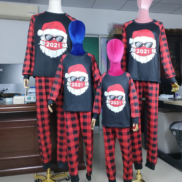 Family matching Christmas pajamas with a Santa Claus graphic wearing sunglasses and a '2021' mask, paired with red and black buffalo plaid pants.