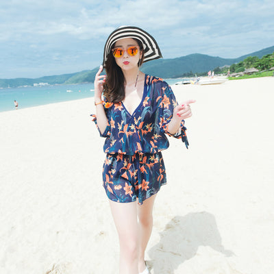 Man wearing navy blue swim shorts with a vibrant orange and green floral pattern, standing on a sunny beach. - Image 4