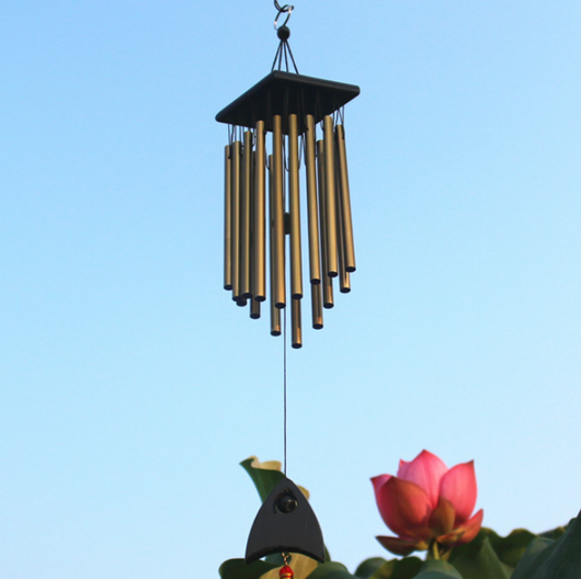 Bronze wind chime with multiple metal tubes hanging from a dark rectangular top, set against green lotus leaves. - Image 6