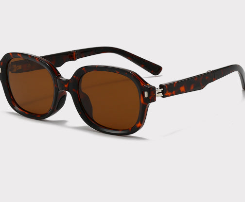 Brown oval sunglasses with dark lenses and thick frames, featuring visible silver hinges on a light gray background. - Image 15