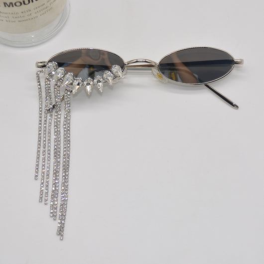Silver oval-frame sunglasses with mirrored lenses and glamorous rhinestone tassels on one side, held by a gloved hand. - Image 4