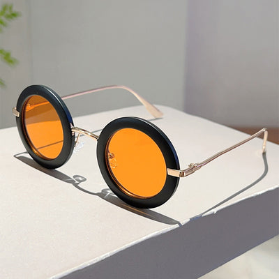 Small frame oval fashion sunglasses with black frames and vibrant orange lenses, held by a hand. - Image 24