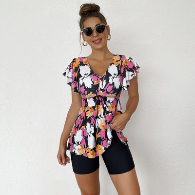 Woman in a blue, black, and white floral print swim top with flutter sleeves and black swim shorts. - Image 3